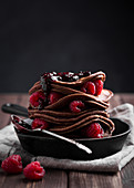 Stack of chocolate pancakes with raspberries and jam