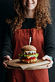 Girl in apron holding wooden board with big homemade cheeseburger