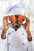Handsome african american chef covering eyes with tomatoes at restaurant kitchen