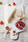 Ein Stück Brie mit Mohn-Crackern und Erdbeermarmelade auf Marmorbrett