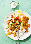 Breaded cod fillet with fried potatoes and cucumber and tomato salad