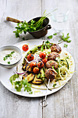 Meatball skewers with cumin served with grilled vegetables and a dip