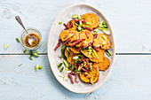 Roasted sweet potatoes with bacon strips and spring onions