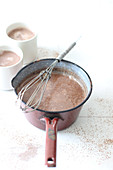 Homemade hot chocolate in a saucepan and cups