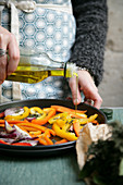 Woman pouring olive oil on cut vegetables