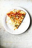 Ein Stück Pizza mit Schinken, Peperoni und Käse auf Pappteller