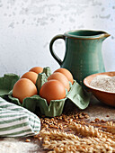 Still life with eggs in an egg carton, flour, cereal and a jug