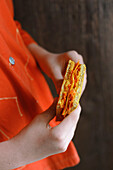 Hände halten orangefarbenes Sandwich