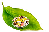Various capsules of food supplements loose in small bowls on a plant leaf