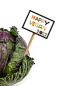 A sign with inscription 'Happy Vegan 2022' stuck in a cabbage head