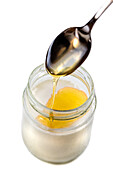 Spoon full of honey pouring into a yoghurt on a white background.
