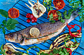 Grilled sea bass on a barbecue grill surrounded by vegetables