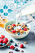 Adding milk to a bowl of muesli with summerfruit and chocolate chips