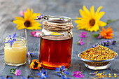 Miel, pollen de fleurs et gélée royale alignés sur un fond gris parsemé de fleurs.