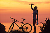 Female mountainbiker cooling herself with water after cycling tour, coastline, Mallorca, Spain