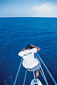 Jugendlicher sitzt auf Schiffsbug und betrachtet die Wellen, Karibisches Meer