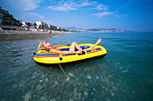 Junge Frau entspannt sich im Gummiboot, Strand, Baie des Anges, Nizza, Côte D'Azur, Frankreich