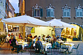 Menschen sitzen an Tischen eines Restaurants auf der Piazza Tre Novembre am Abend, Riva del Garda, Gardasee, Trentino, Italien, Europa