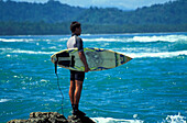 Surfer standing at rock and looking over sea, Puerto Viejo, Costa Rica, Caribbean, Central America