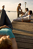 Four young people sitting on boardwalk and drinking beer, Munich, Bavaria