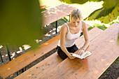 Young woman reading book in beer garden, Munich, Bavaria