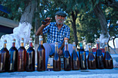 Mature man with bottles of wine beneath a tree, Perissa, Santorin, Cyclades, Greece, Europe