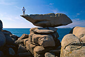 Mann steht auf einem Fels im Sonnenlicht, Côte de Granit Rose, Ploumanach, Bretagne, Frankreich, Europa