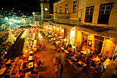 Menschen sitzen nachts vor einer Bar auf der Promenade, Hydra, Saronische Inseln, Griechenland