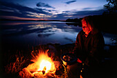 Woman sitting on campfire, Lake Sommen, Ostergotland, Sweden
