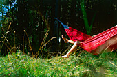 Young woman relaxing in hammock, legs hanging over side