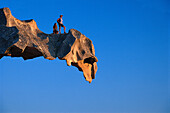 Two hikers on a rock ledge at Capo d´Orso, a bear shaped rock, Sardinia, Italy