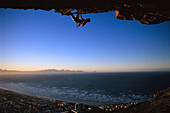 Rock climber climbing an overhang, Muizenberg Bay, South Africa