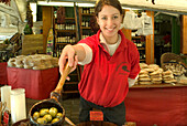 Woman at market stand of outdoor market Viktualienmarkt offering olives, Munich, Bavaria, Germany