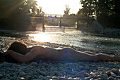 Naked man lying at Isar riverbank in the sunlight, Flaucher, Munich, Bavaria, Germany