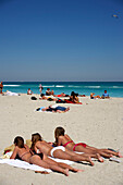 Drei junge Frauen liegen in der Sonne, Strandleben, Art Deco Altstadt, South Beach, Miami, Florida, USA