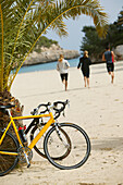 Three people on a cycle tour on the beach at cala santanyi, Majorca, Balearic Islands, Spain