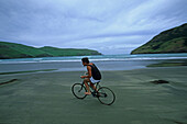 Man on old bicycle on sand beach, NZ, man riding old bicycle on beach at Pigeon Bay, Banks Peninsula, Fahrradfahrer am Strand, Pigeon Bay Banks Halbinsel
