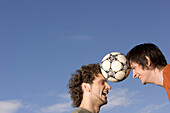 Two young man juggling soccer ball between their heads