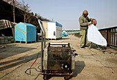 Homeless, living boxes in Tokyo, Japan, Homeless community on the banks of the Sumida River, neighbourhood help, hair cutting with electricity from a generator Obdachlose, notdürftige Schutzbauten, Pappkarton-Architektur, Plastikplanen, Slum, Obdachlosigk