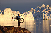 Frau mit Mountainbike, trägt Fahrrad und betrachtet den Aussicht, Ilulissat, Greenland