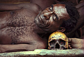 Ein Mann ruht auf einem Totenschädel, Irian Jaya, Papua Neuguinea