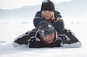 Junge liegt auf dem Rücken seines Vaters im Schnee