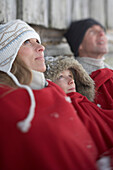 Parents and son leaning on wooden hut, warming with red blanket