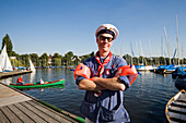 Fisher smiling at camera, Man wearing a Fischerhemd a typical shirt of a fisher, , water wings and a sailor's hat standing on a jetty of Bobby Reich and smiling at camera, Hamburg, Germany