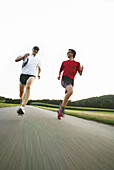 Two young men jogging on country road