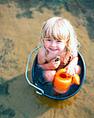 Little girl sitting in wash bowl, holding watering pot