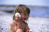 Little girl holding shell to ear on the beach