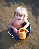 Little girl sitting in wash bowl, holding watering pot