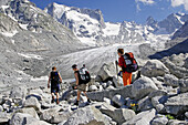 Four people hiking towards a glacier. In the background impressive mountains. Forno Glacier, Bergell, Graubuenden, Grisons, Switzerland, Alps.