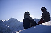 Young man and woman sitting on snow, looking mountain panorama, Kuehtai, Tyrol, Austria